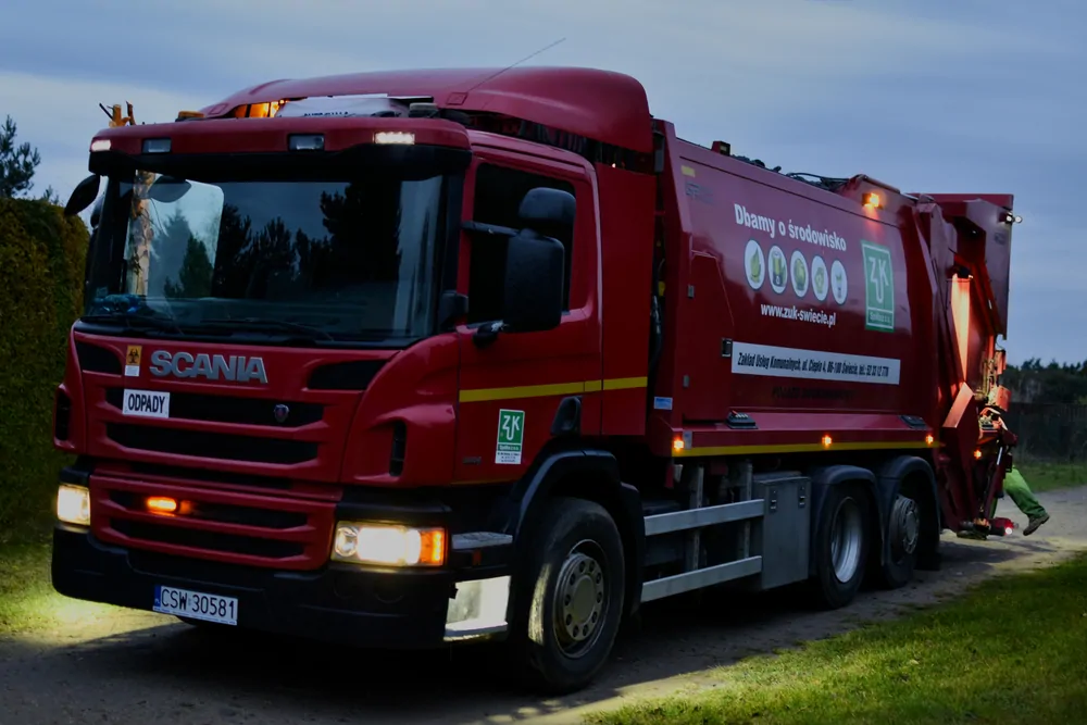 Czerwona śmieciarka Scania o zmierzchu na trasie odbioru