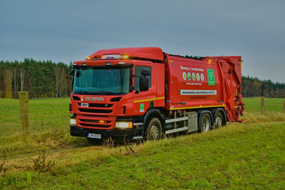 Czerwona śmieciarka Scania na łące przy lesie