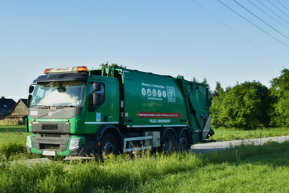 Zielona śmieciarka Volvo na drodze wiejskiej o wschodzie słońca