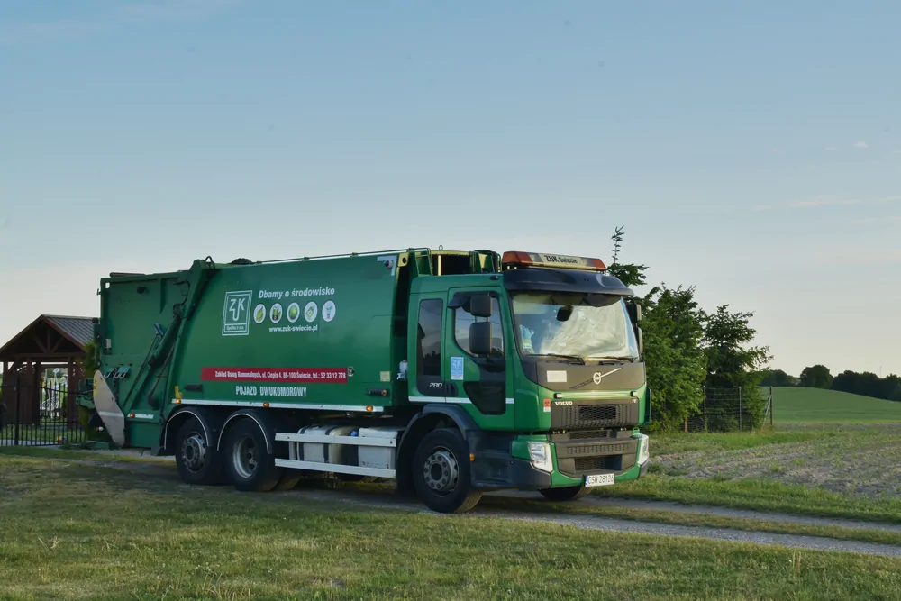Zielona śmieciarka Volvo zaparkowana przy placu zabaw
