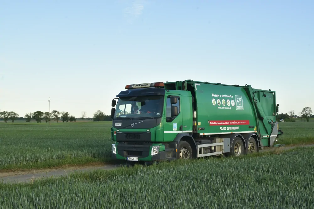 Zielona śmieciarka Volvo na polnej drodze wśród zboża