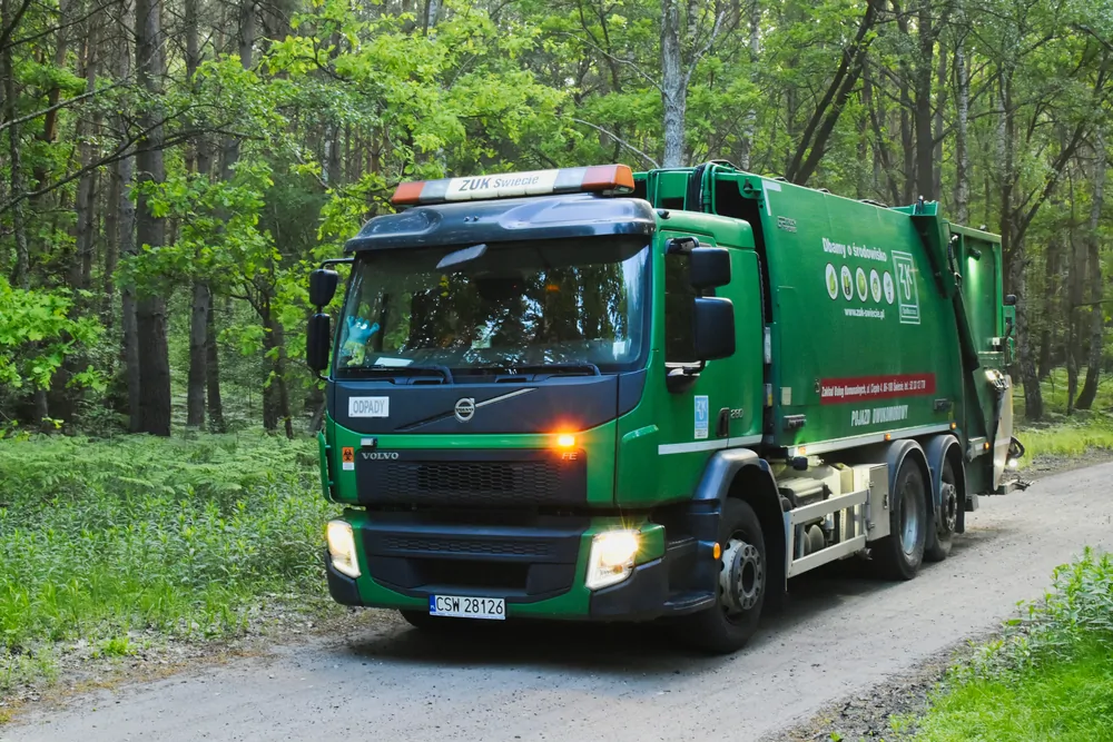 Zielona śmieciarka Volvo na leśnej drodze