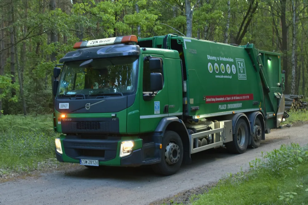 Zielona śmieciarka Volvo w lesie, ujęcie z boku