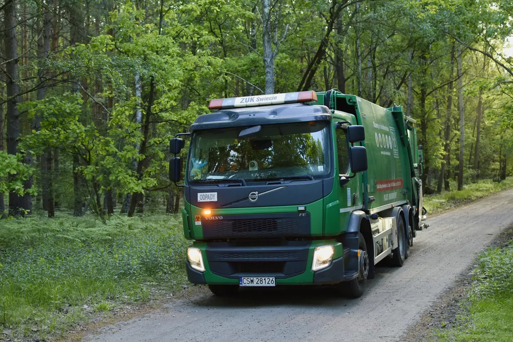 Zielona śmieciarka Volvo na leśnej drodze na wprost