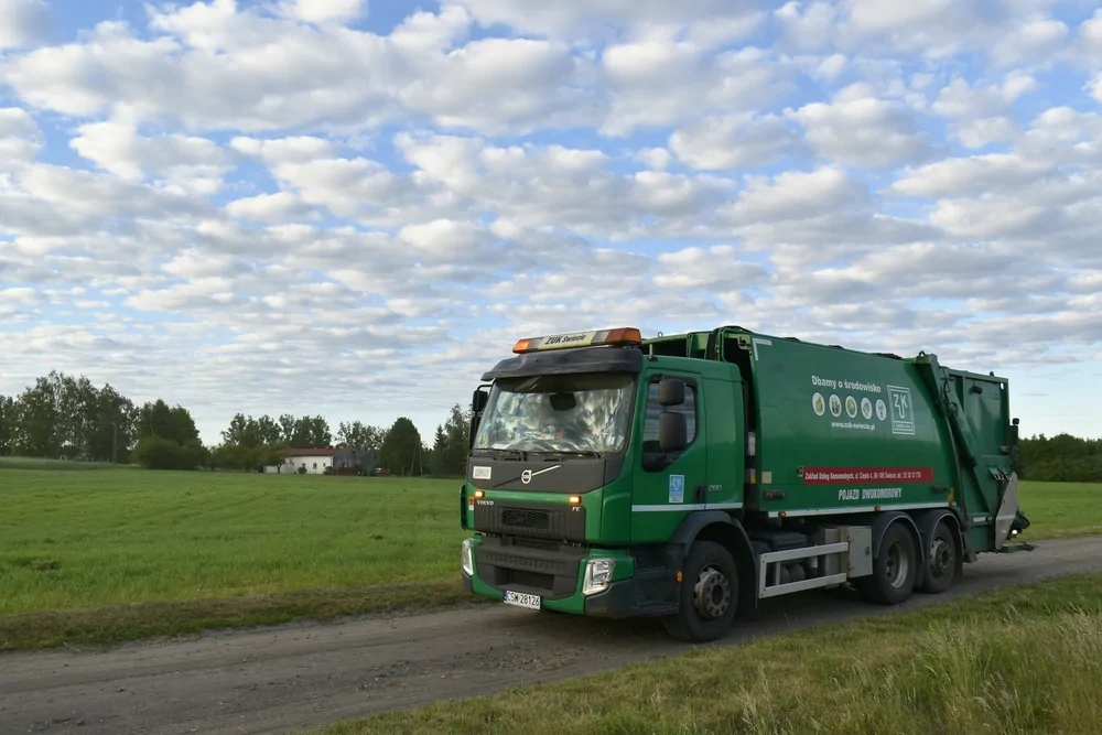 Zielona śmieciarka Volvo na drodze polnej pod chmurami
