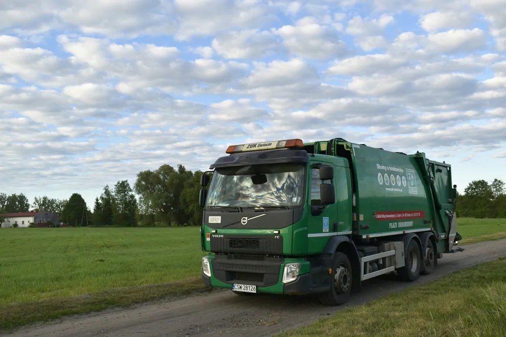 Zielona śmieciarka Volvo na drodze polnej