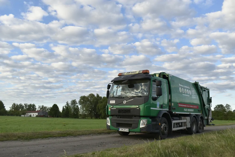 Zielona śmieciarka Volvo w krajobrazie wiejskim
