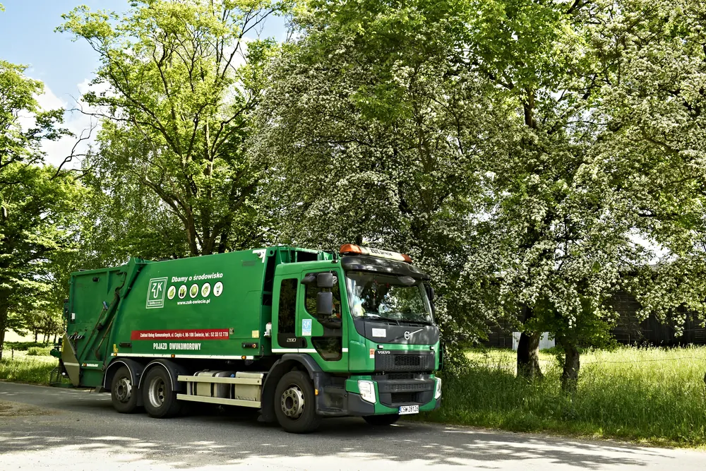 Zielona śmieciarka Volvo pod kwitnącymi drzewami