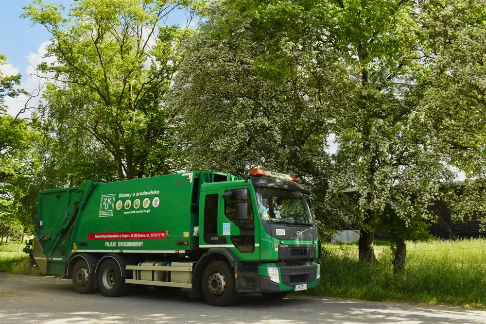 Zielona śmieciarka Volvo wśród wiosennej zieleni